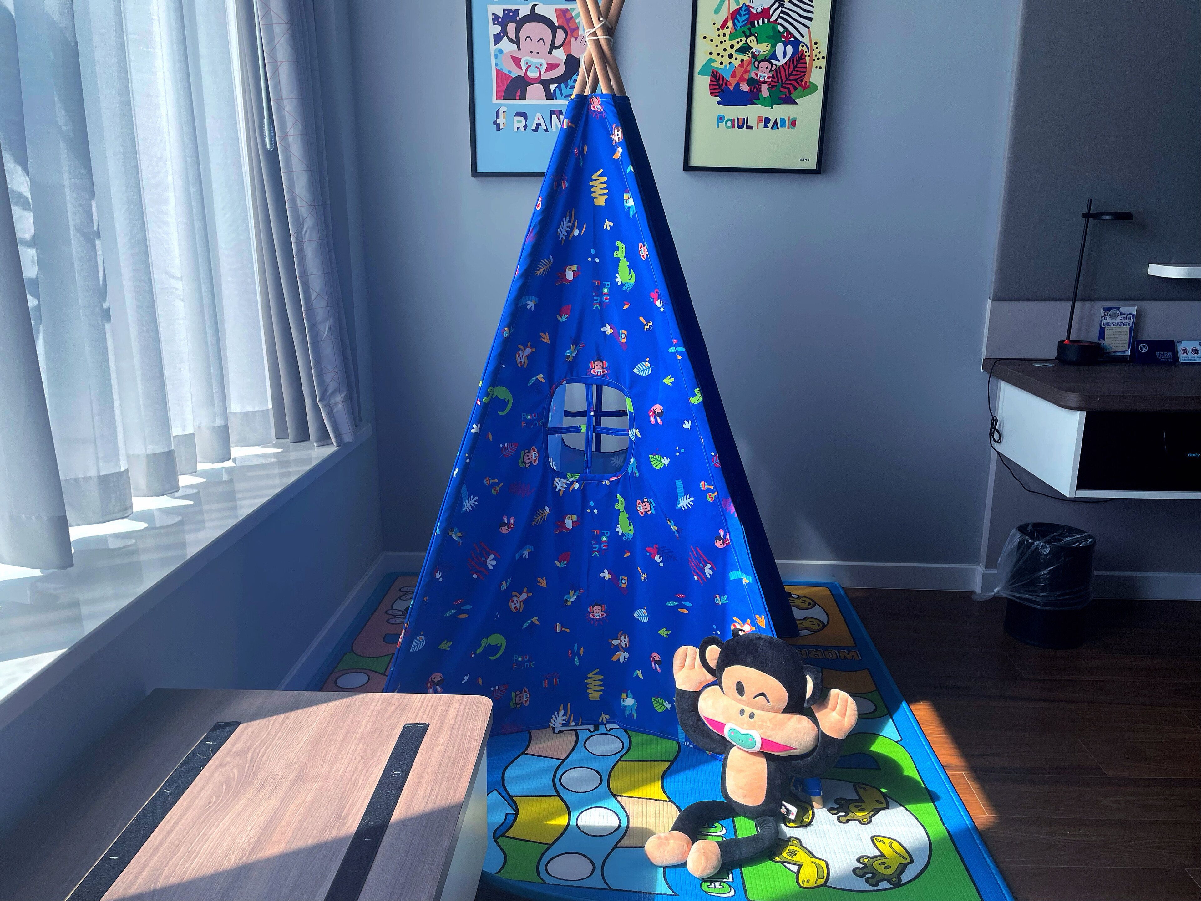 A room with a blue play tent, a plush monkey toy, and a colorful play mat.