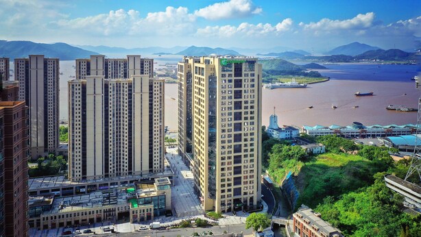 A high-rise building with a modern architectural design, situated near a body of water with boats and a bridge. - Holiday Inn Express Zhoushan Dinghai by IHG (Zhoushan)