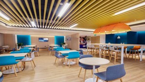 A modern dining area with wooden tables and blue chairs, a bar area with stools, and a ceiling with linear lighting. - Holiday Inn Express Zhoushan Dinghai by IHG (Zhoushan)