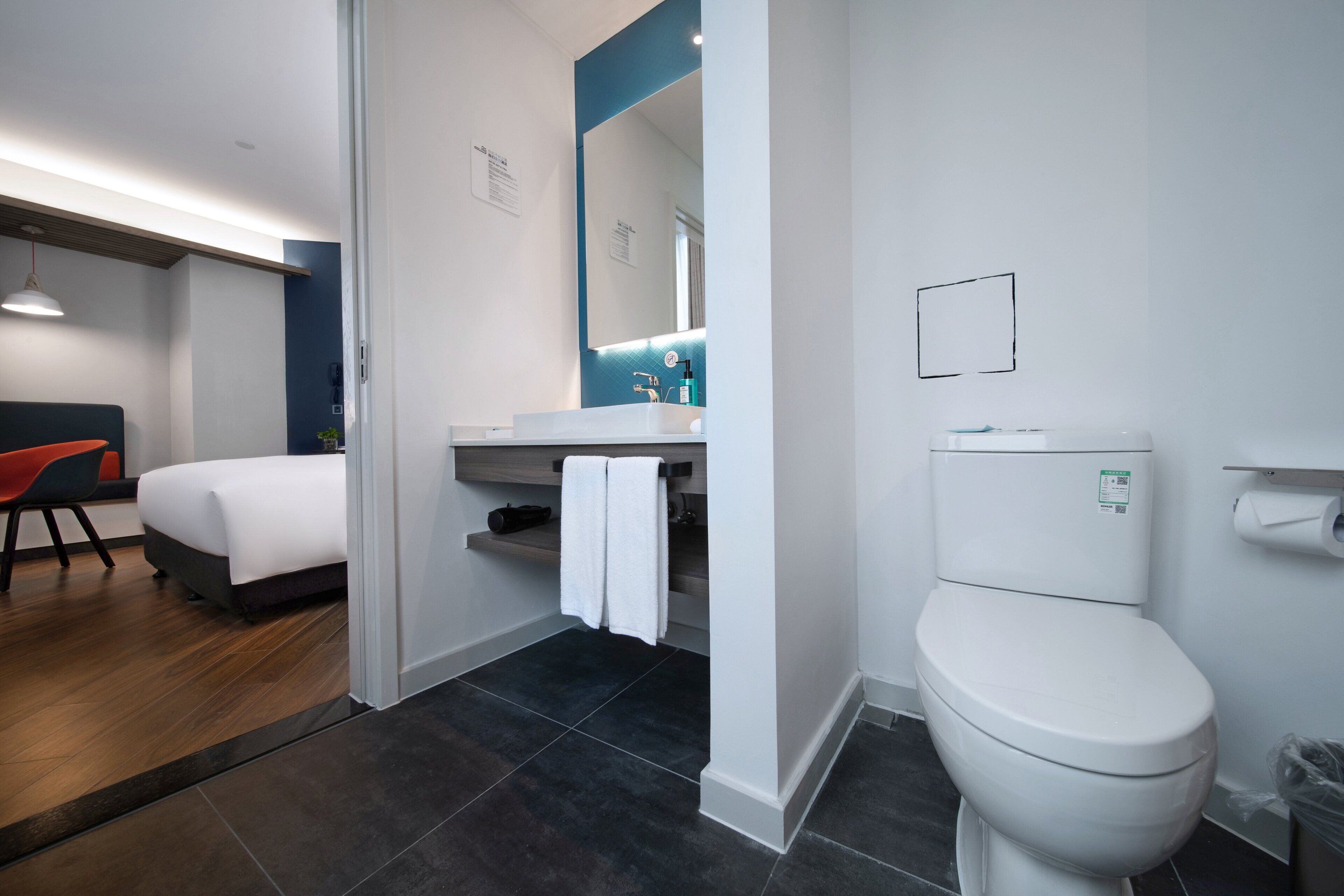A modern hotel room with a bed, a desk, a bathroom with a toilet, and a shower area.