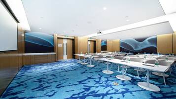 A conference room with a blue carpet, white tables, and chairs, equipped with water bottles.