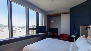 Hotelkamer met een groot bed, een bureau met een computer, een stoel en uitzicht op het water door grote ramen.