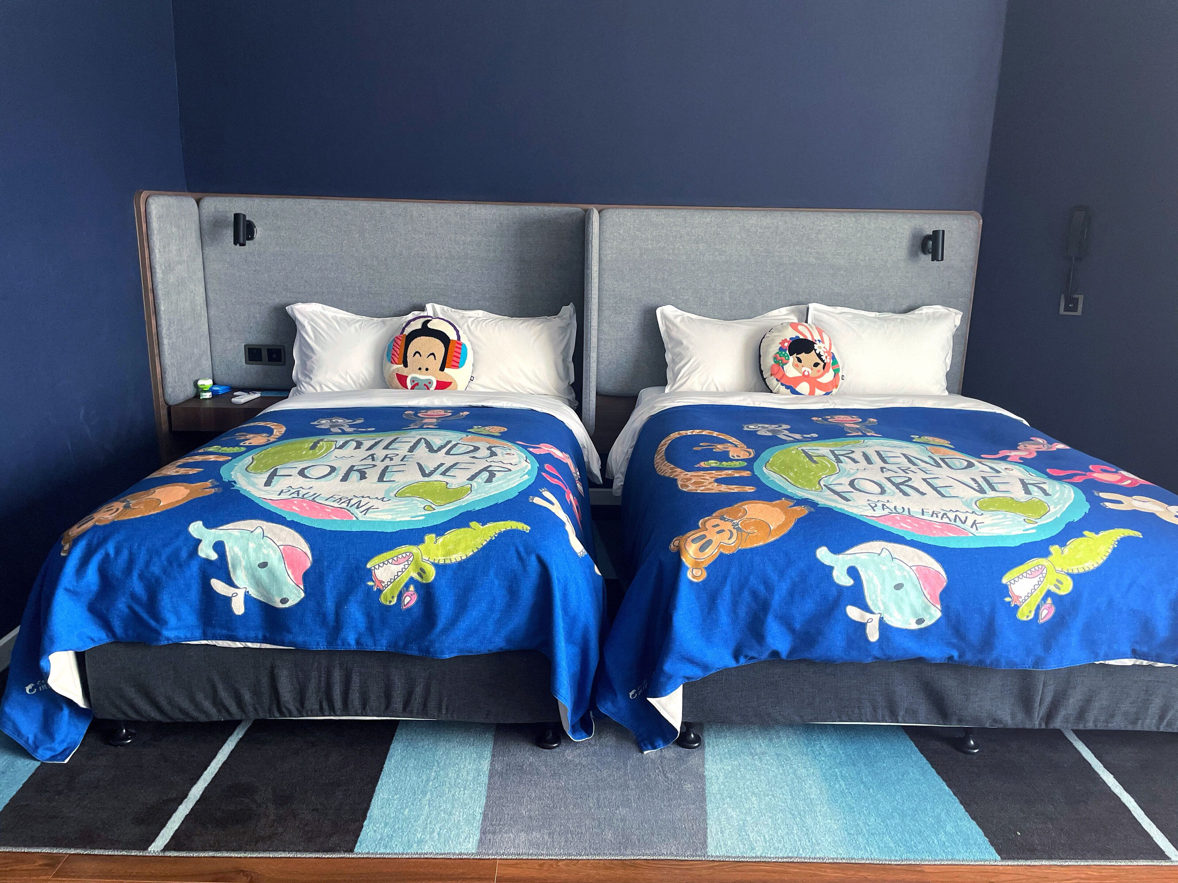 Una cama doble con dos almohadas, cada una con un personaje de caricatura. El edredón tiene un diseño colorido con el texto "Friends Forever" y "Paul Frank".