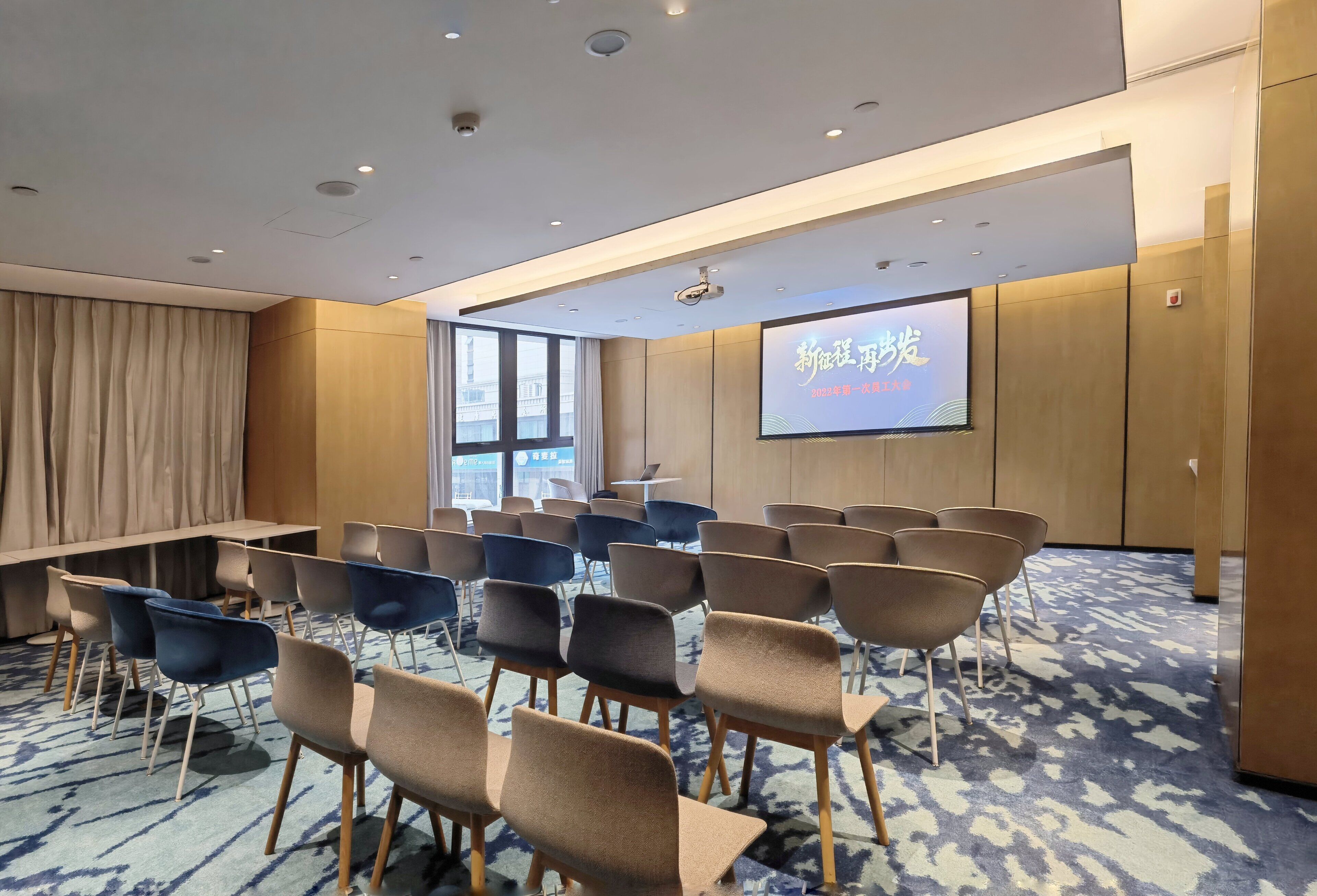 Une salle de conférence avec des rangées de chaises, un grand écran et une table.
