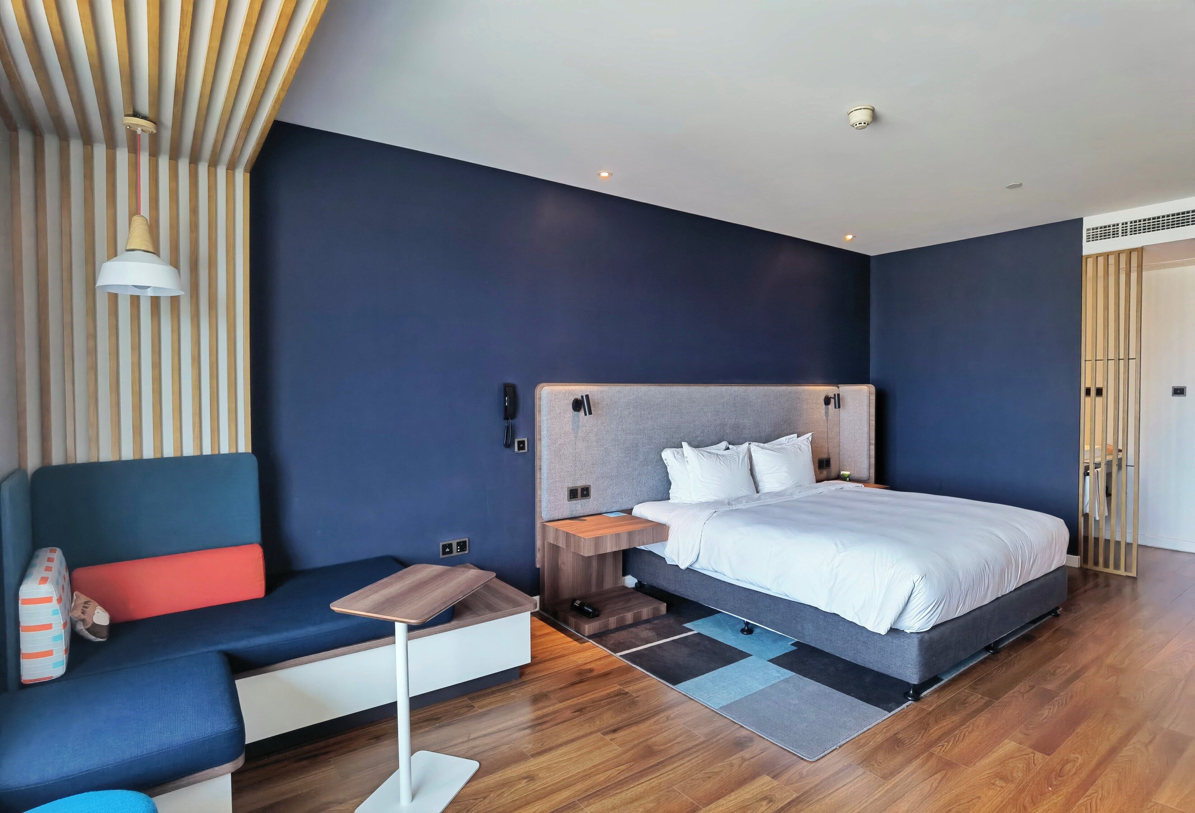A modern bedroom with a bed, bedside table, and a seating area with a sofa and a small table.