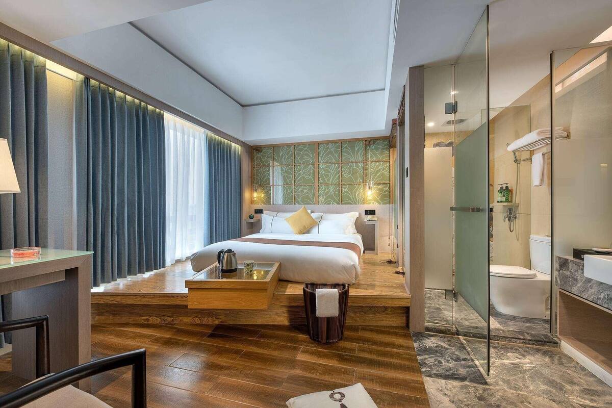 Una habitación de hotel moderna con cama, mesita de noche, lámpara y vistas al baño.