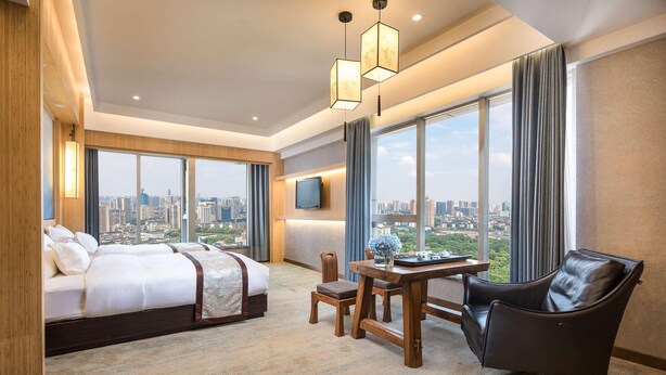 Habitación de hotel con cama, escritorio, silla y ventana grande con vista a la ciudad.