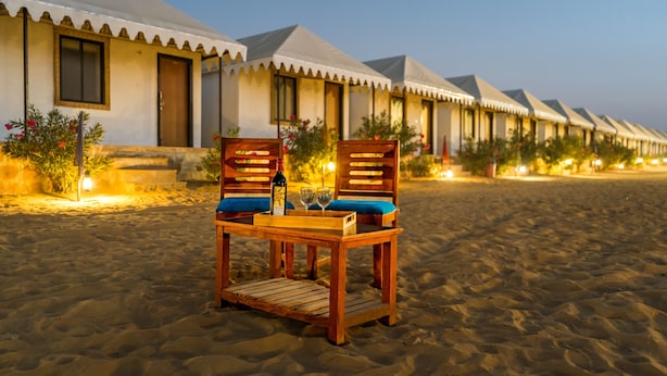 A row of beachside villas with a wooden table and chairs in the foreground. - Style Desert Camp Jaisalmer (Jaisalmer)
