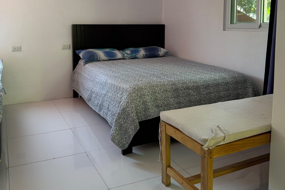 A small, neatly arranged bedroom with a bed, a wooden table, and a window.