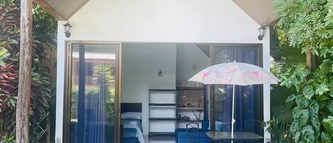 A modern house with a covered patio, a dining area with a table and chairs, and a kitchen visible through the glass doors.