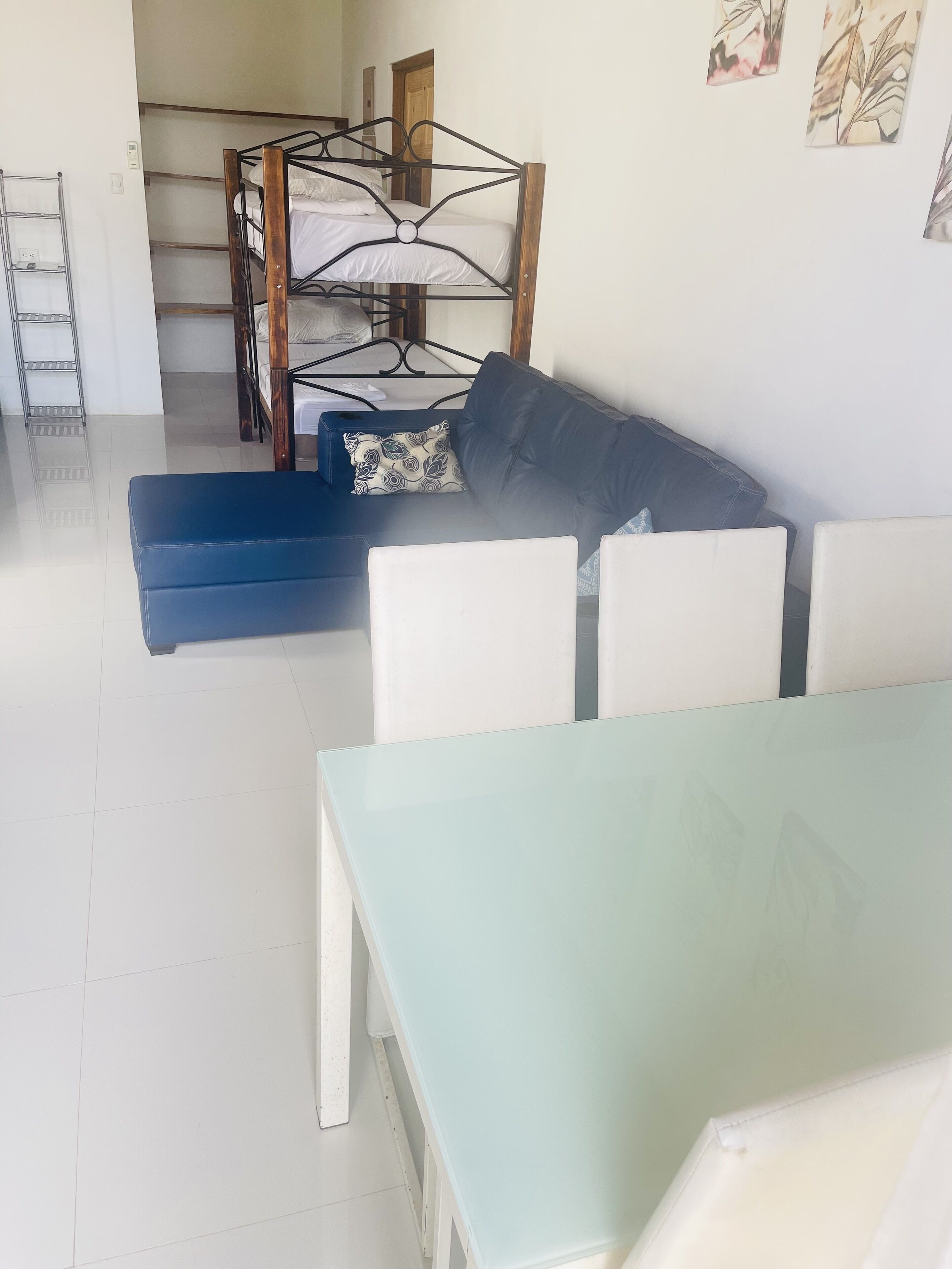 Ein Zimmer mit einem Etagenbett, einem blauen Sofa, einem Glastisch und weißen Stühlen.