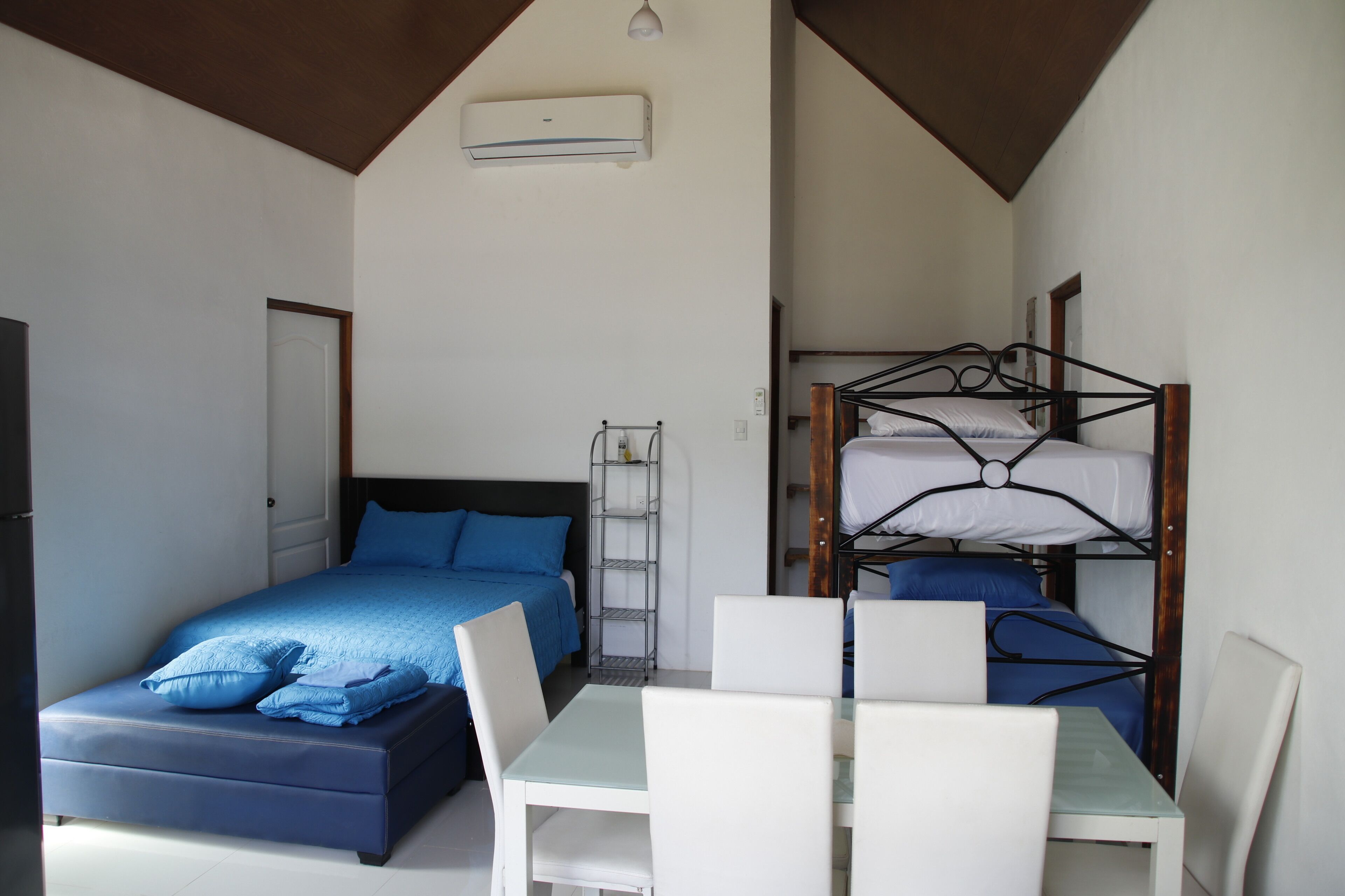 A bedroom with a single bed, a bunk bed, a table with chairs, and a ceiling fan.