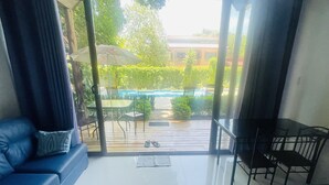 Un salon moderne avec un canapé bleu, une petite table et une vue sur une piscine et un jardin, grâce à de grandes fenêtres.
