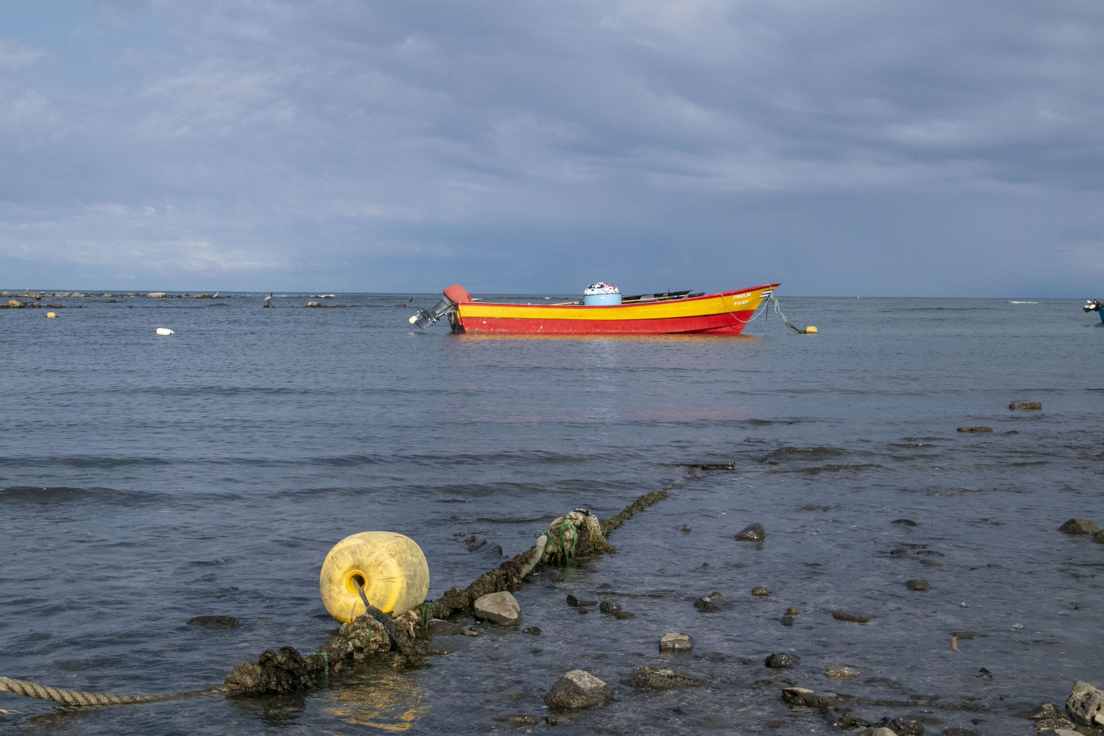 Ein Boot liegt an einer felsigen Küste, das Wasser ist ruhig und der Himmel bewölkt.