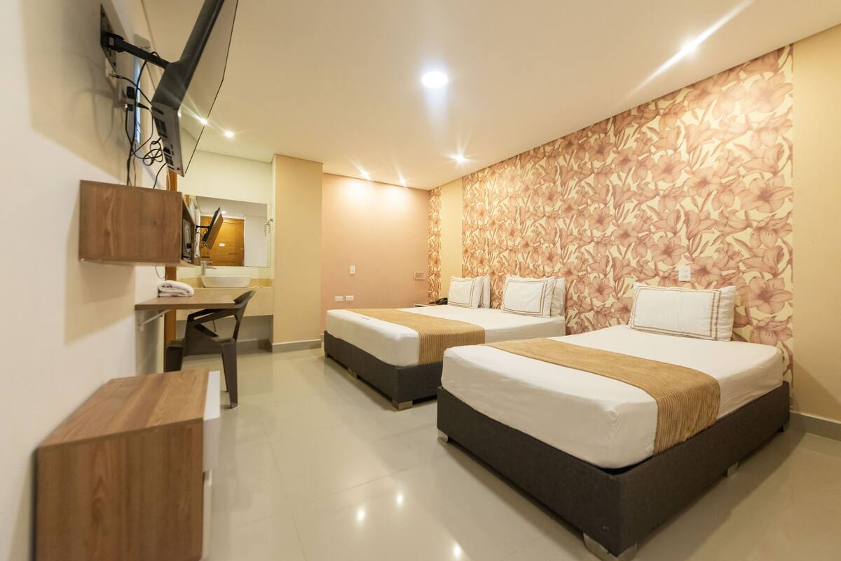 A hotel room with two beds, a desk, and a mirror.