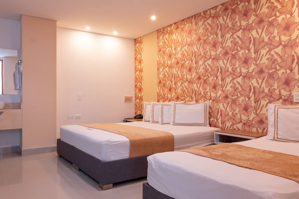 A hotel room with two beds, a bathroom, and a floral wallpaper design.