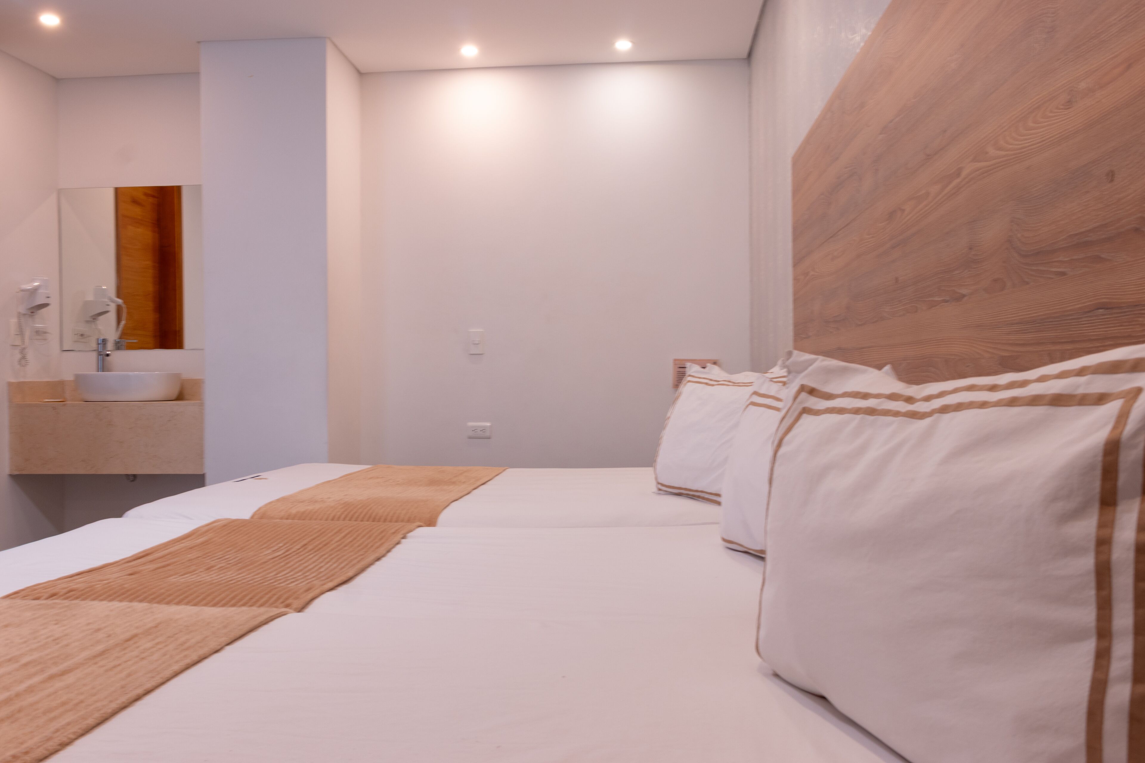 Una habitación de hotel moderna con una cama grande, cabecera de madera, lavamanos integrado y un espejo encima.
