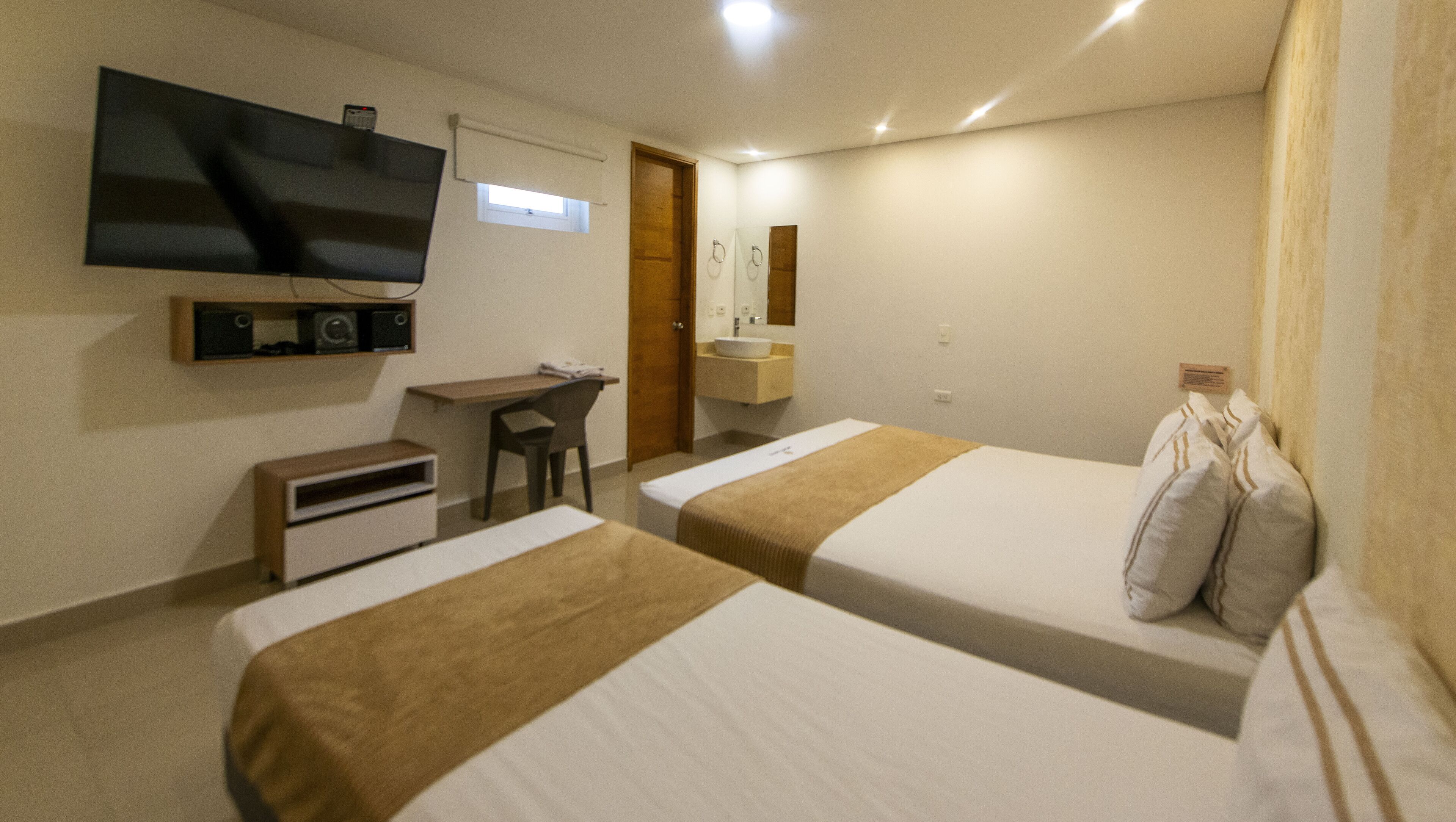 A hotel room with two beds, a desk, a television, a sink, and a mirror.