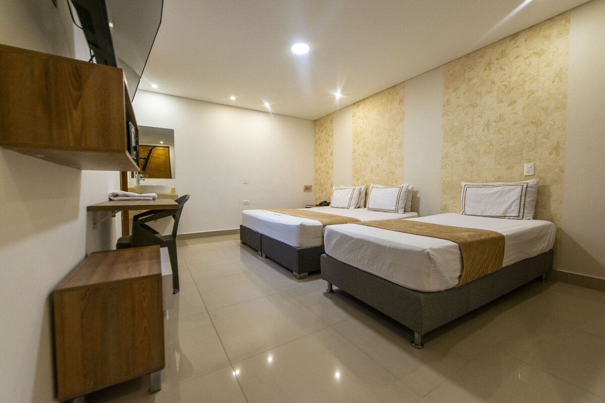 A hotel room with two single beds, a desk with a chair, and a small wooden cabinet.