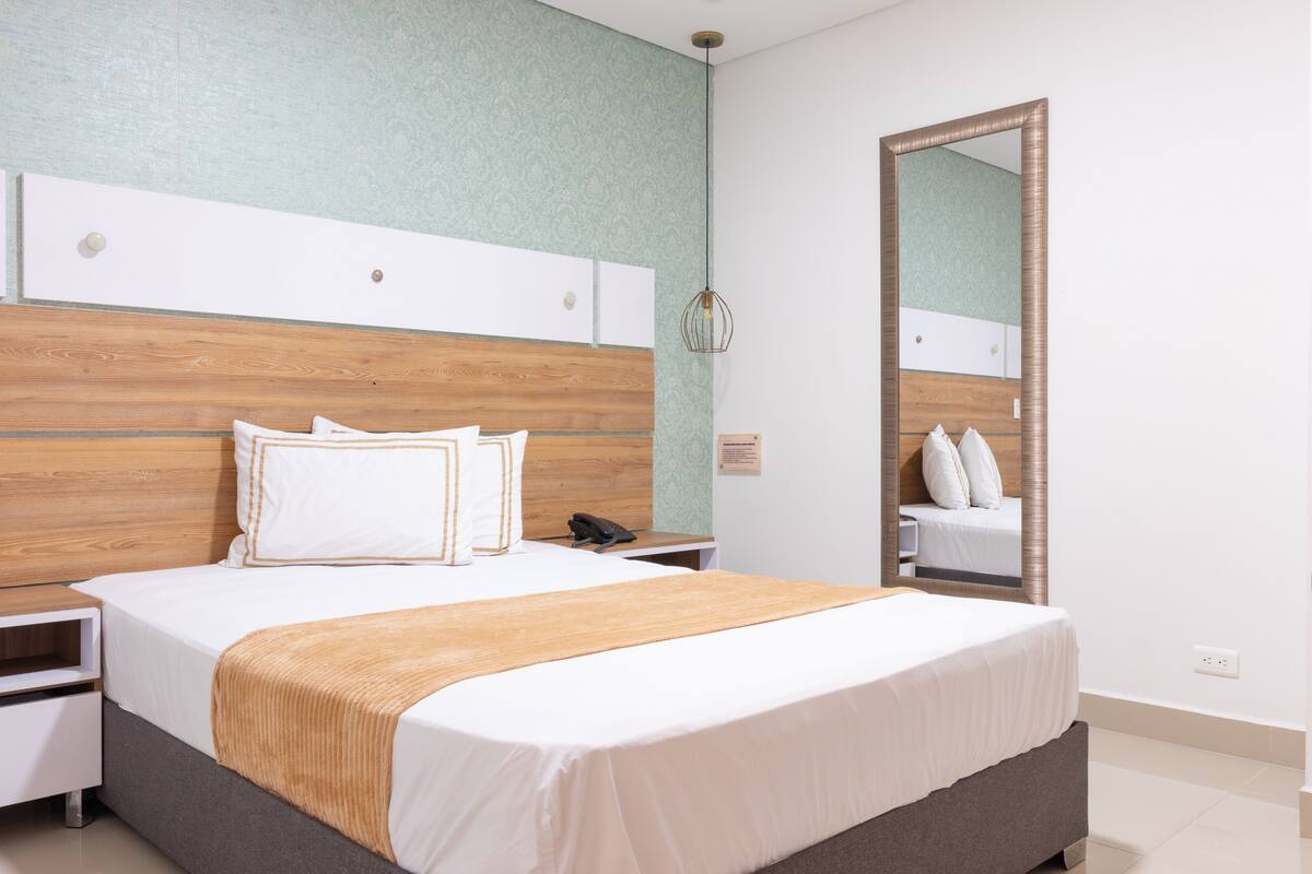 A neatly made bed with a wooden headboard, a bedside table with a lamp, and a mirror on the wall.