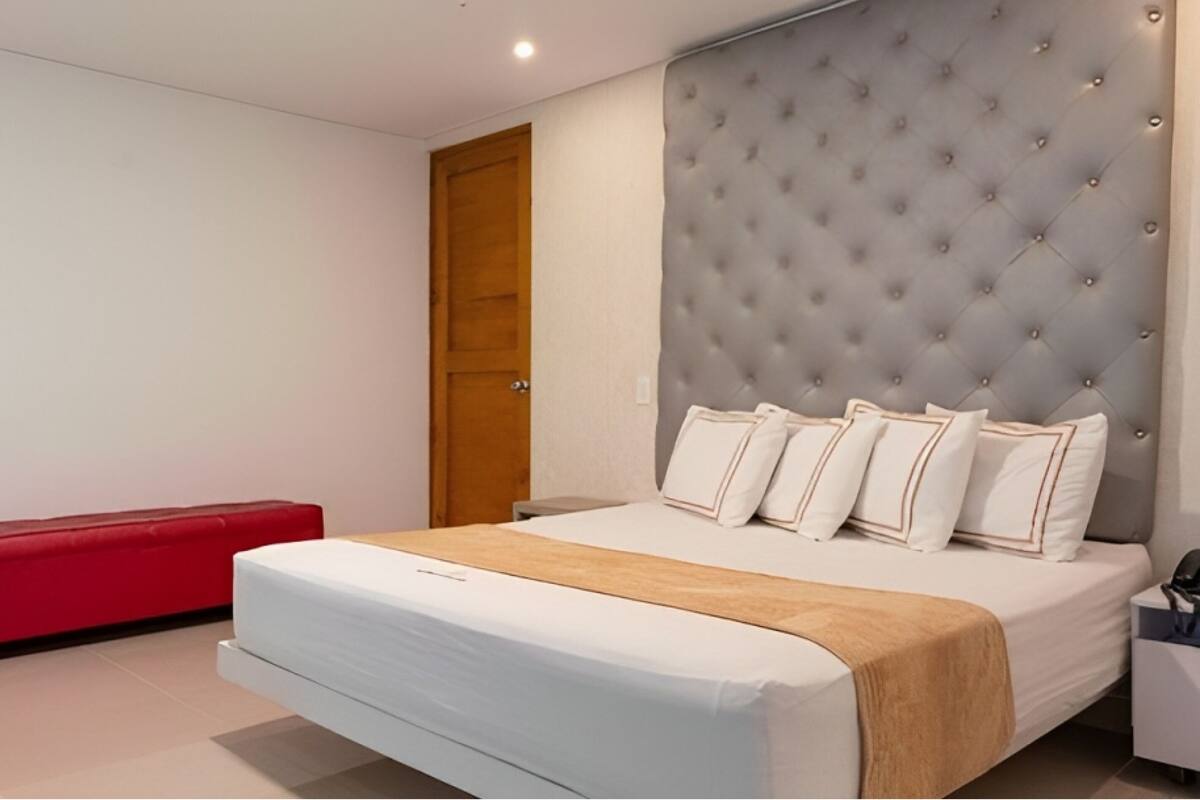 A modern bedroom with a large bed, a red bench, and a tufted headboard.