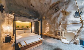 Une chambre confortable avec un lit à baldaquin, un fauteuil suspendu et une petite table de chevet.