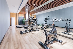 Un gimnasio con bicicletas estáticas y cintas de correr, suelo de madera y un diseño moderno en el techo.