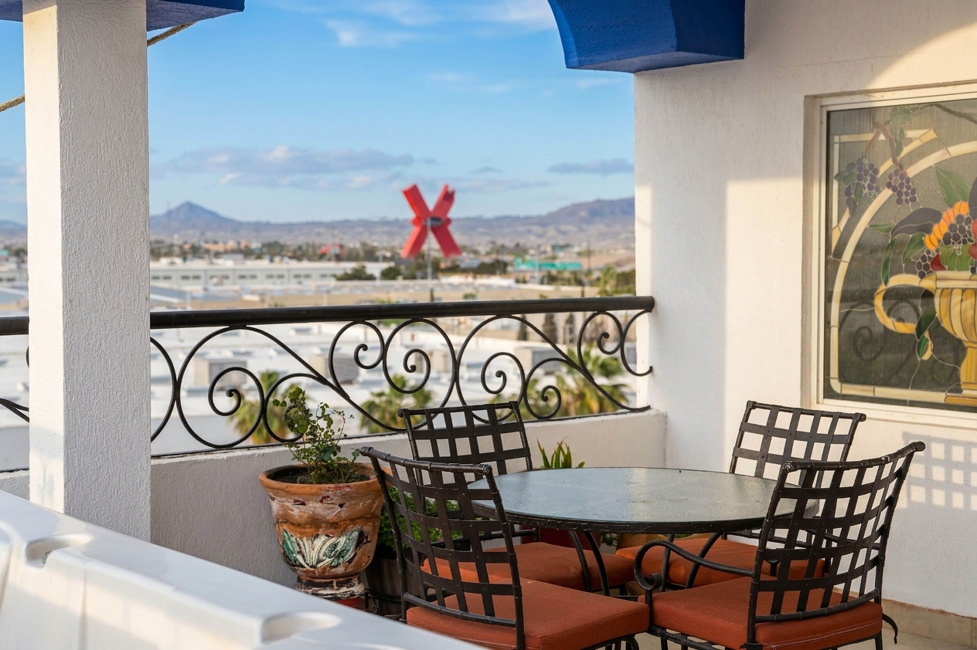 A balcony with a table and chairs, a potted plant, a red X sign, and a painting.