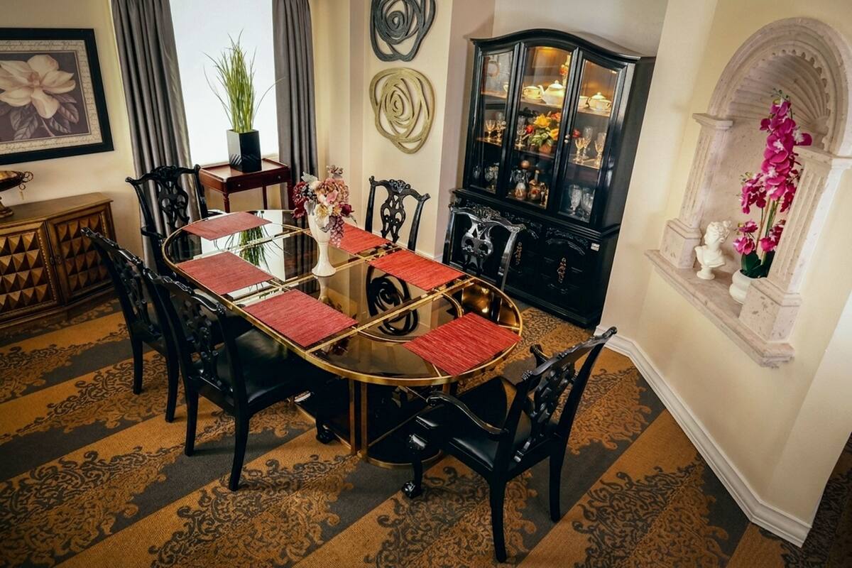 A dining area with a round table, black chairs, red placemats, and a black cabinet with glass doors.