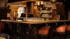 Un espace bar avec un comptoir en bois, des verres suspendus et des tabourets de bar rembourrés.