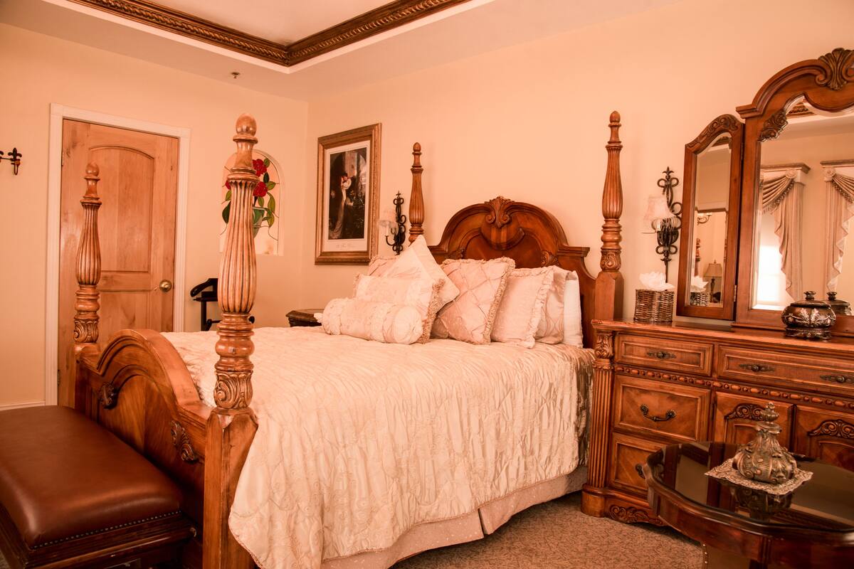 A traditional bedroom with a four-poster bed, a wooden bench, a dresser, and a mirror.