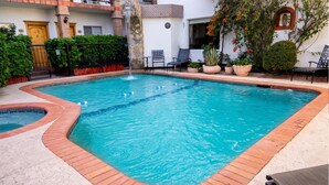 Une piscine bordée de briques, un petit jacuzzi et des plantes en pot.