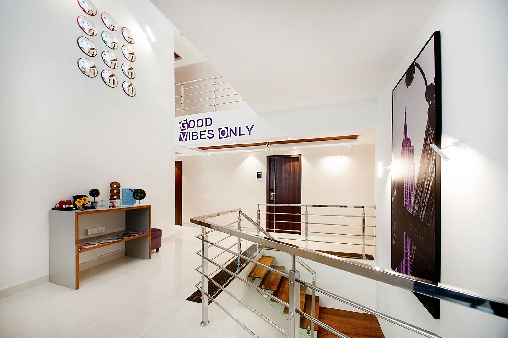 Un interior moderno con una escalera, un cartel que dice 'GOOD VIBES ONLY' y un póster con un paisaje urbano.
