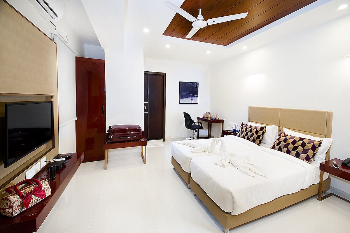 A modern hotel room with a large bed, a desk, a television, and a ceiling fan.