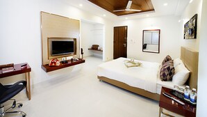 A modern hotel room with a large bed, a desk, a TV mounted on the wall, and a ceiling fan. - Raj Residency (Bengaluru)