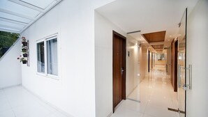 A modern hotel corridor with a glass door, a window with potted plants, and a clean, tiled floor. - Raj Residency (Bengaluru)