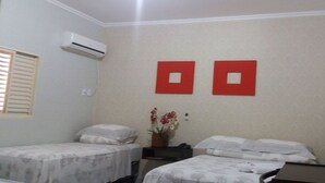 A room with two beds, a small table, a vase with flowers, and two red square decorations on the wall. - Vitor Hotel II (Chapadão do Céu)