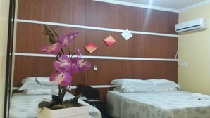 A bedroom with two beds, a wooden headboard, a potted orchid, and a wall-mounted air conditioner. - Vitor Hotel II (Chapadão do Céu)