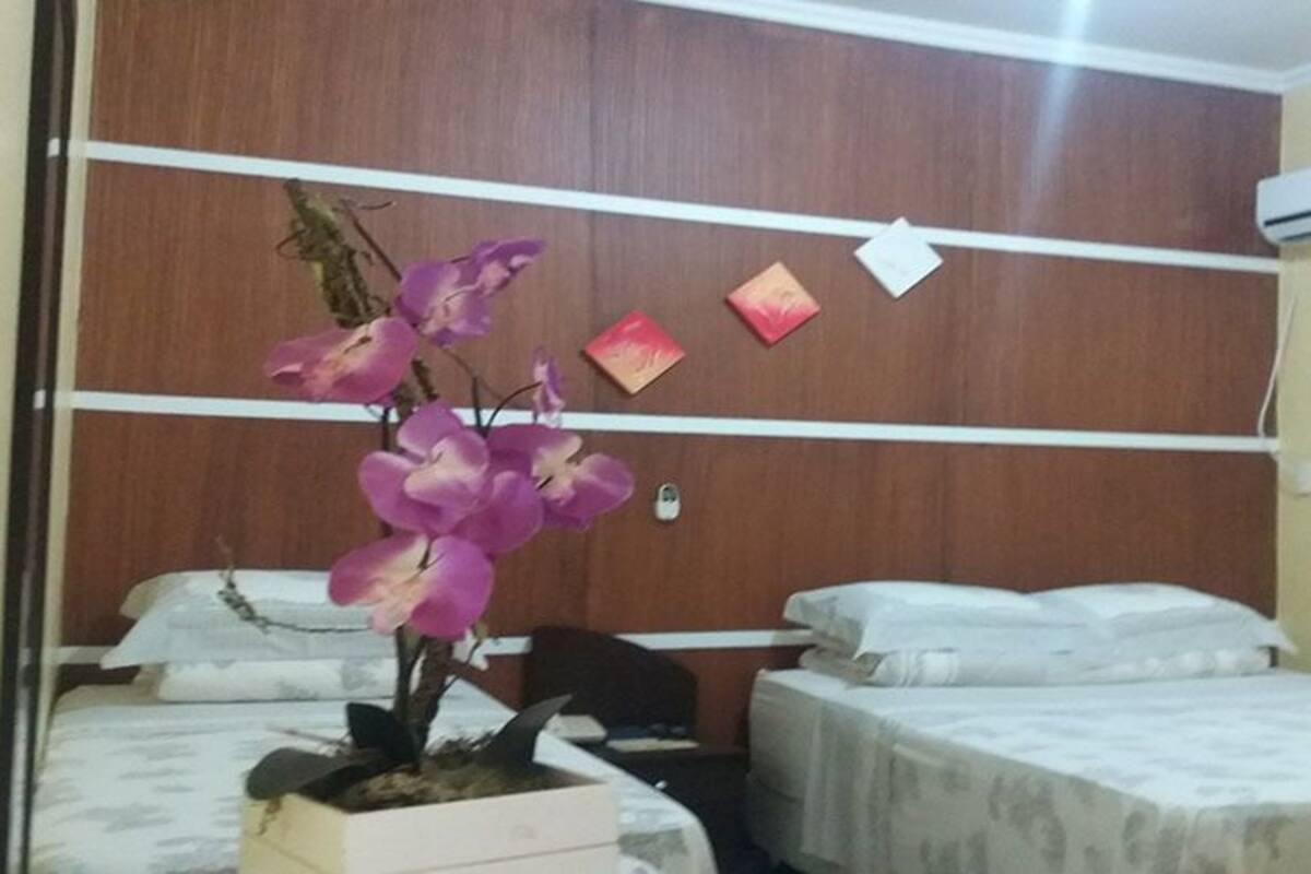 Une chambre avec deux lits, une tête de lit en bois, une orchidée en pot et un climatiseur fixé au mur.