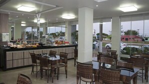 A restaurant with a buffet counter, wicker chairs, and large windows offering a view of the street. - Vitor Hotel II (Chapadão do Céu)
