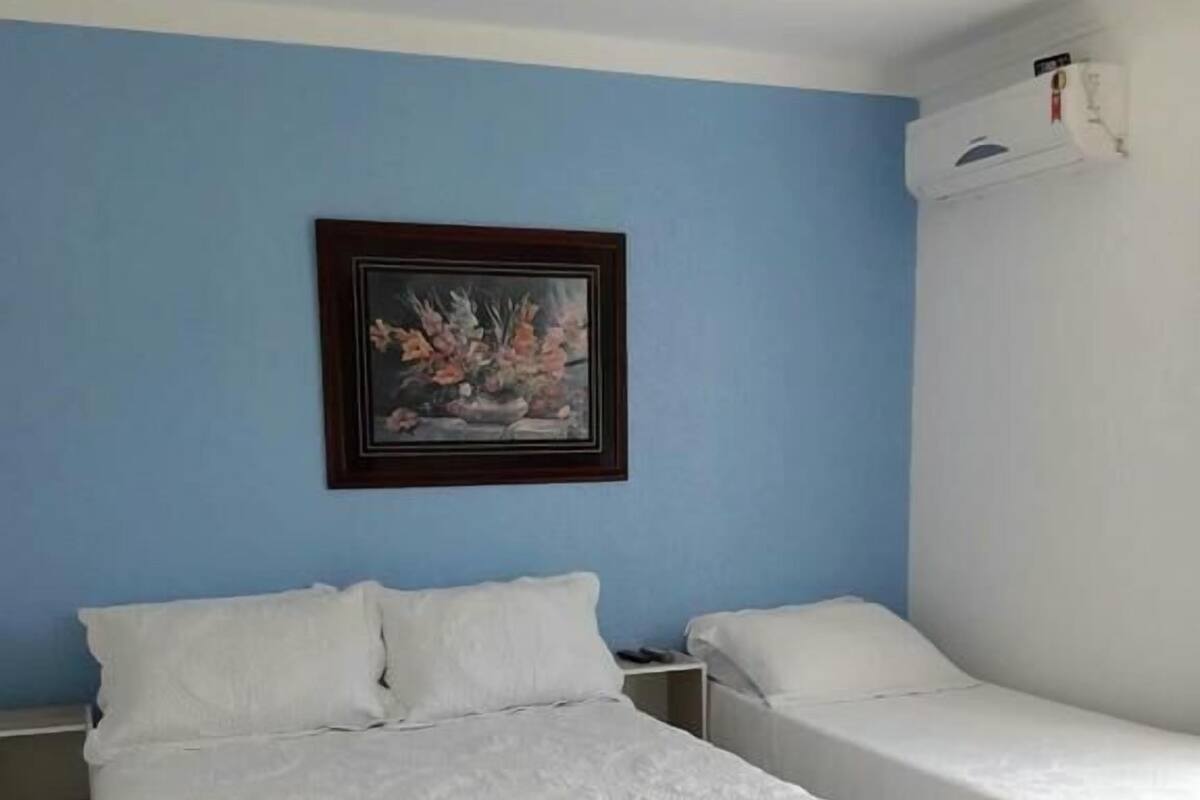 Un dormitorio con una cama grande, dos camas individuales, un ventilador de techo y un cuadro en la pared.