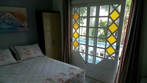 Une chambre à coucher avec un lit, une armoire et une vue sur l’extérieur, visible à travers une porte ornée d’un motif géométrique.