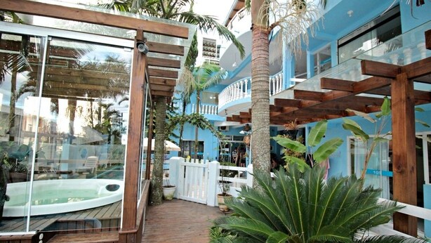 Une terrasse en bois avec un jacuzzi, entourée de palmiers et d’une clôture blanche.