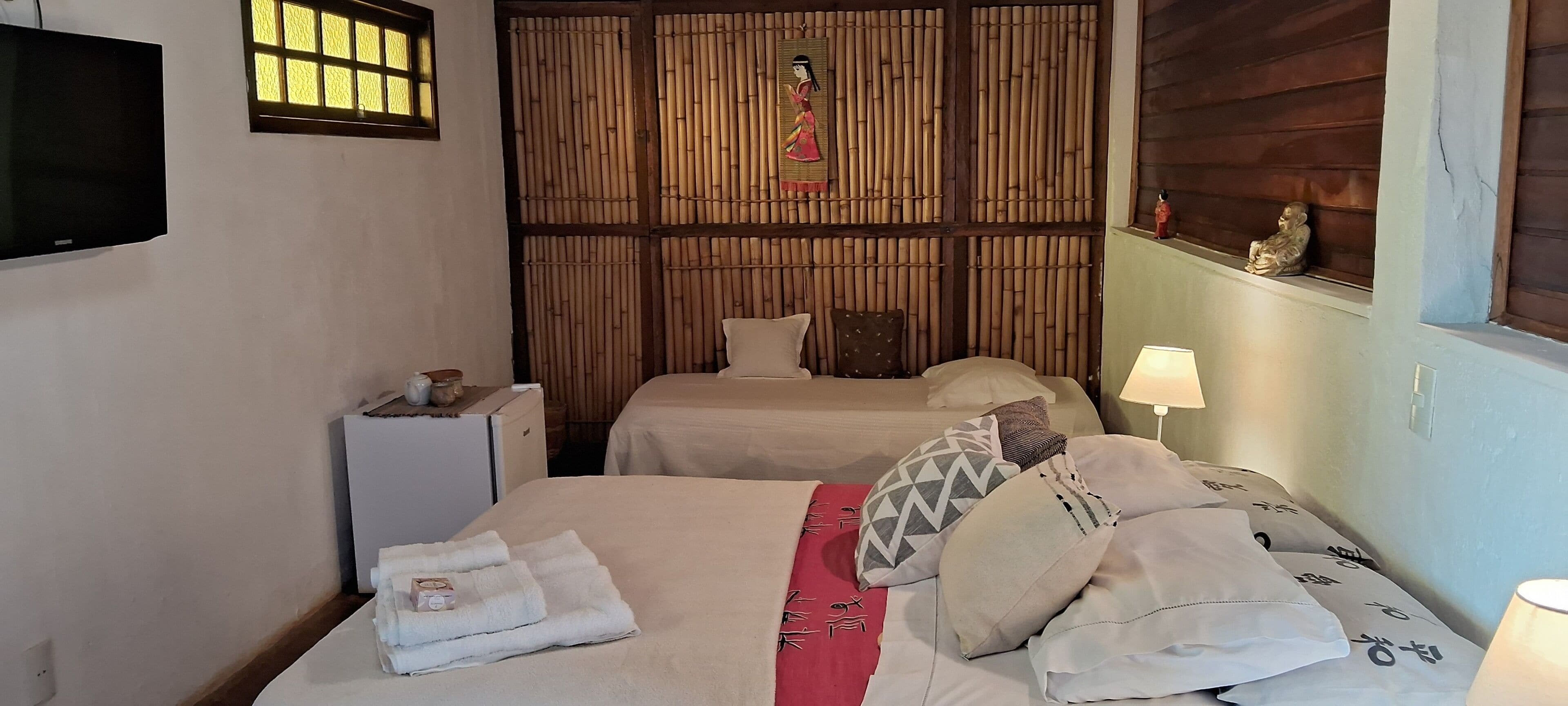 Una habitación con dos camas, un televisor, un panel de bambú en la pared y una pequeña estatua.