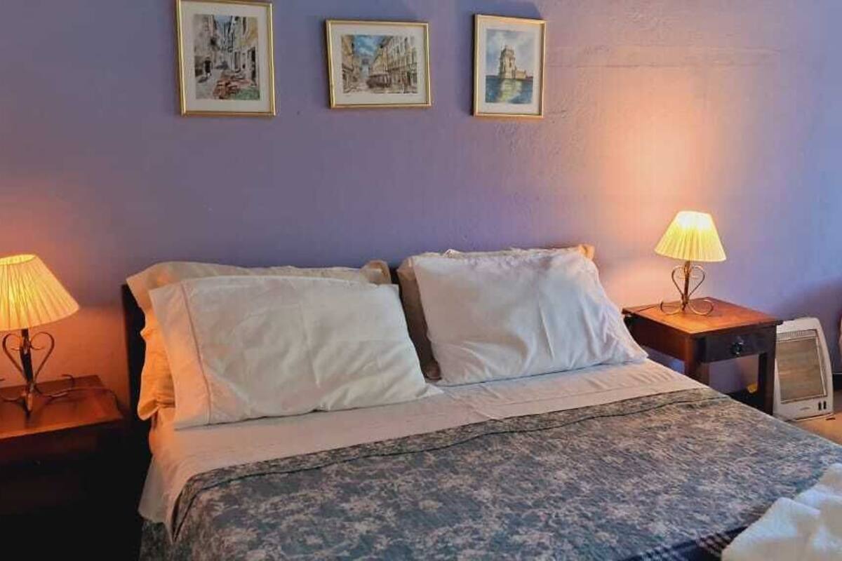 Une chambre avec deux lits, une table de chevet avec une lampe et une commode avec une lampe. Trois tableaux encadrés ornent le mur.