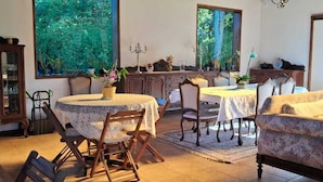 A dining area with round tables and chairs, a cabinet with glass doors, and a view of greenery through large windows. - Chalé na Montanha (Cunha)
