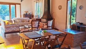 A cozy living room with a fireplace, a dining area with wooden furniture, and a kitchen with a brick oven. - Chalé na Montanha (Cunha)
