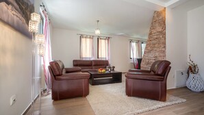 A living room with a brown leather sofa set, a coffee table, and a large window with curtains. - Villa SOA (Razvršje)