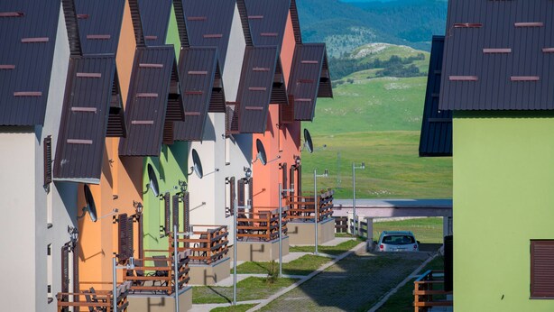 A row of colorful buildings with slanted roofs, outdoor seating areas, and a car parked in front. - Villa SOA (Razvršje)