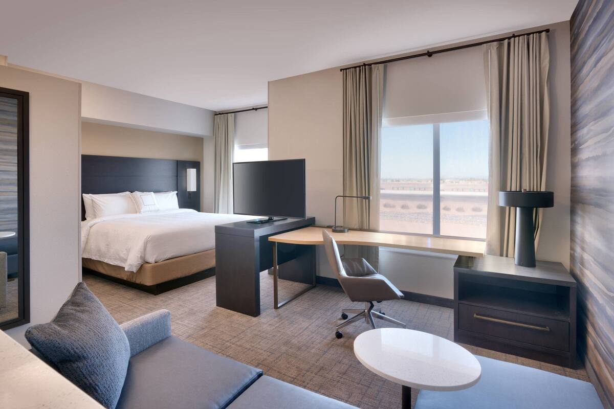 A modern hotel room with a bed, desk, chair, and a small table.